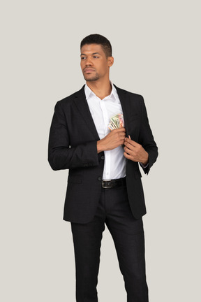 Vorderansicht eines jungen mannes im schwarzen anzug, der banknoten in die tasche steckt