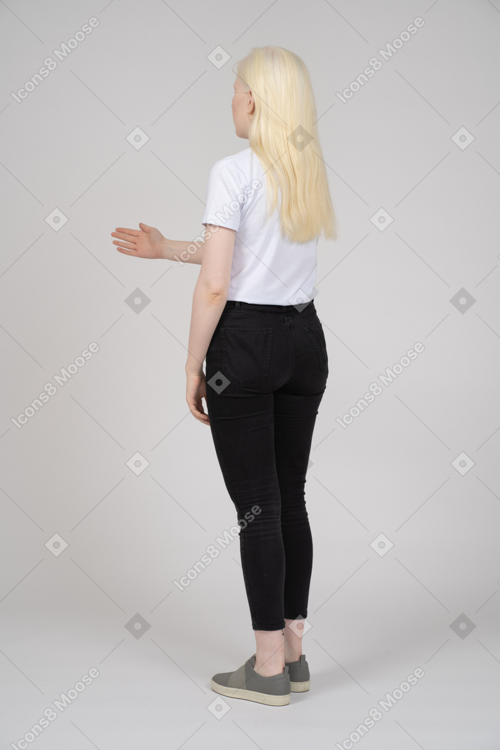 Вид сзади на молодую девушку, стоящую с приветственным жестом руки