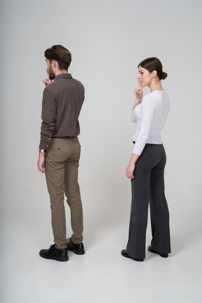 Three-quarter back view of a young couple in office clothing showing silence gesture