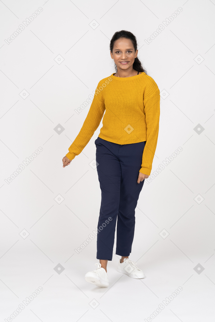 Front view of a happy girl in casual clothes looking at camera and walking forward