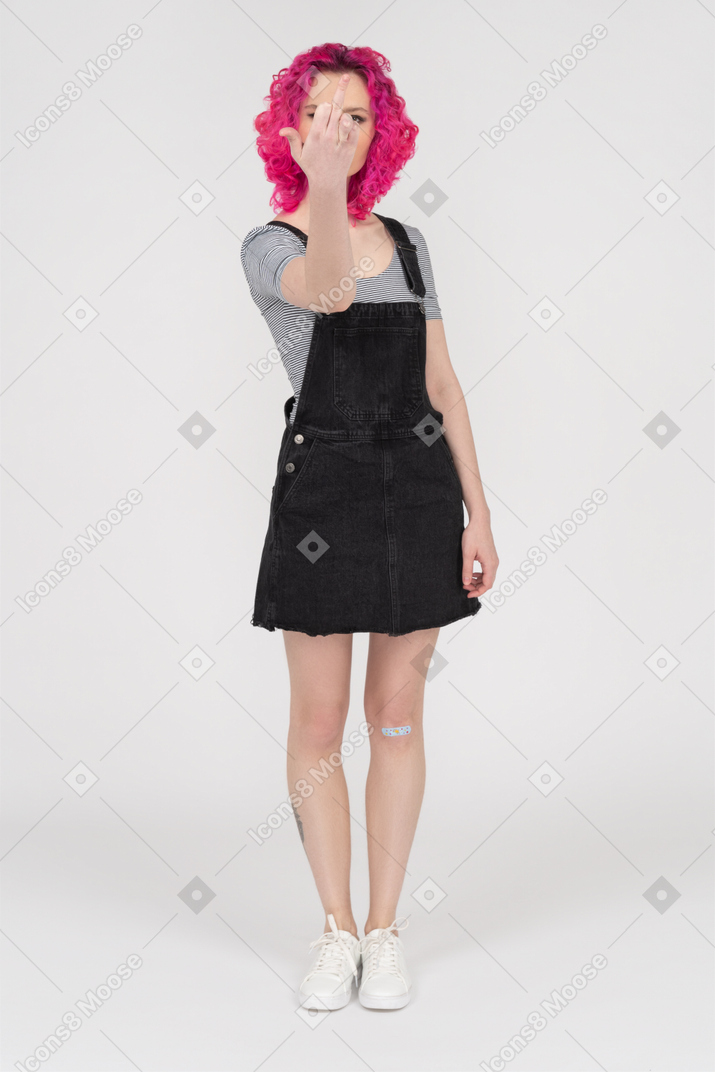Adolescente femminile con i capelli rosa ricci che mostra un dito medio