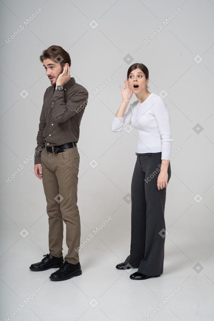Three-quarter view of a young couple in office clothing listening to the rumors
