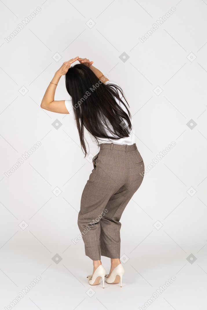 Vista traseira de três quartos de uma jovem assustada de calça tocando a cabeça