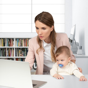 A woman sitting at a desk with a baby in front of a laptop