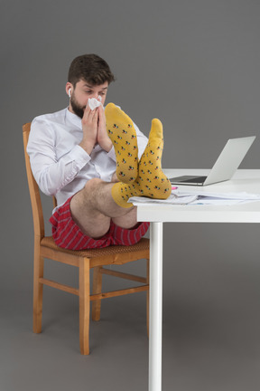 Sick white collar worker wiping his nose and keeping his legs on the table