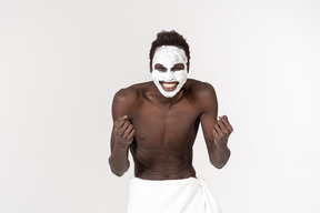 Un jeune homme noir avec une serviette de bain blanche autour de sa taille va sur ses soins du visage