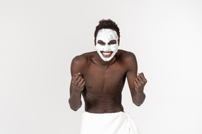 A young black man with a white bath towel around his waist going about his facial care