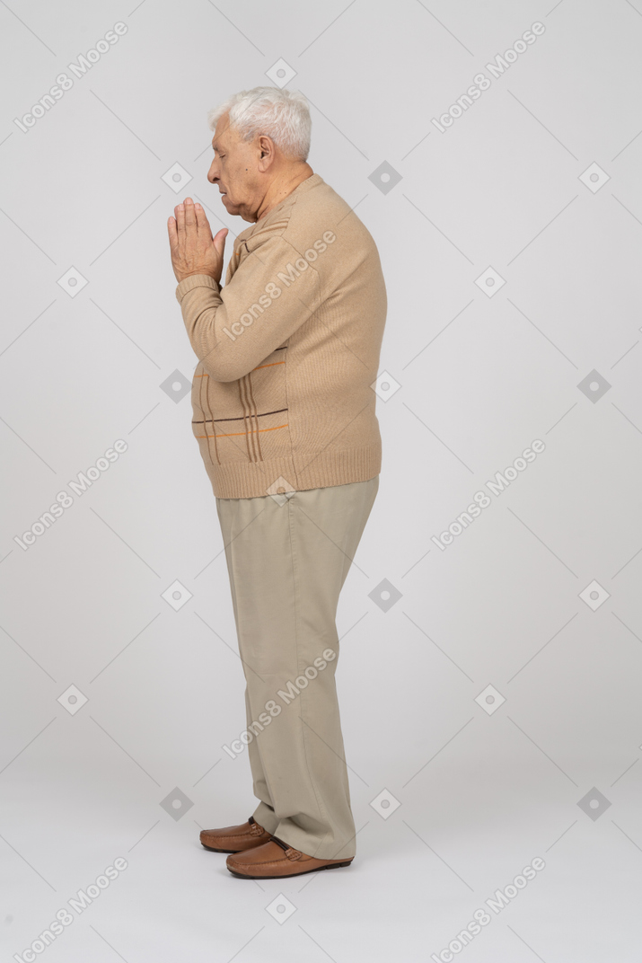 La vista laterale di un vecchio in abiti casual tiene le mani nel gesto di preghiera