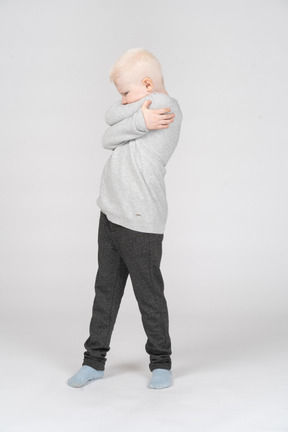 Niño pequeño abrazándose a sí mismo y alejándose