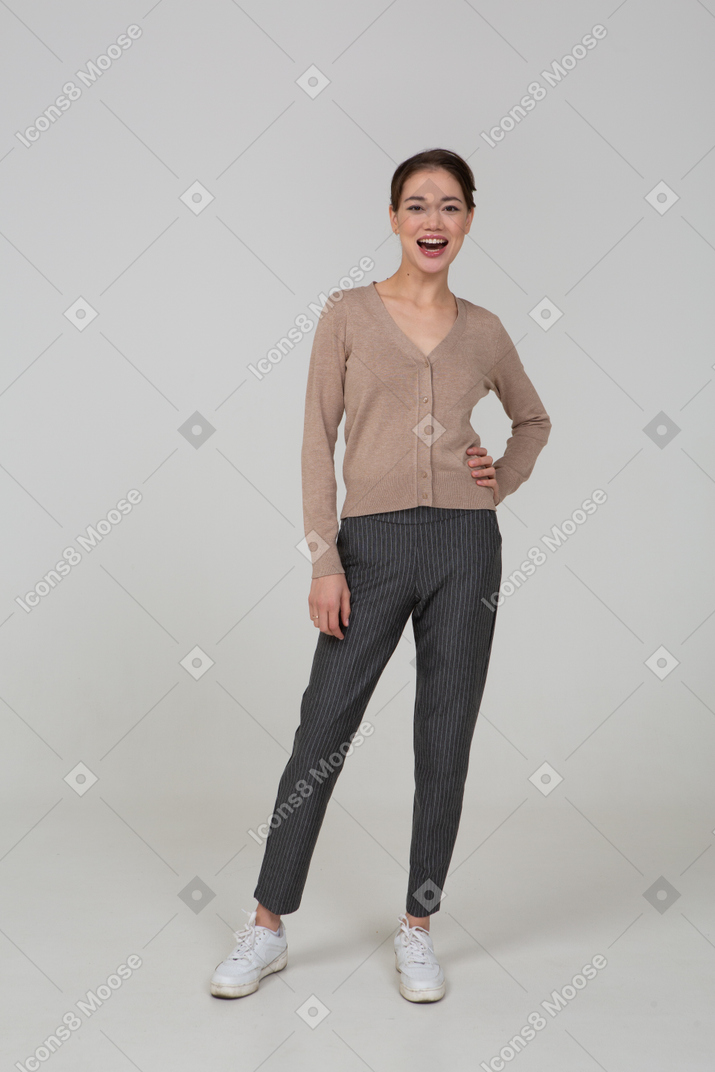 Вид спереди смеющейся женщины в пуловере и штанах, положив руку на бедро