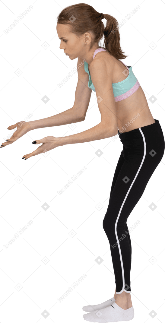 Vue latérale d'une adolescente en vêtements de sport pointant les mains quelque part vers le bas
