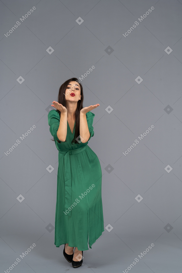 Vista frontal de una joven en vestido verde enviando un beso al aire