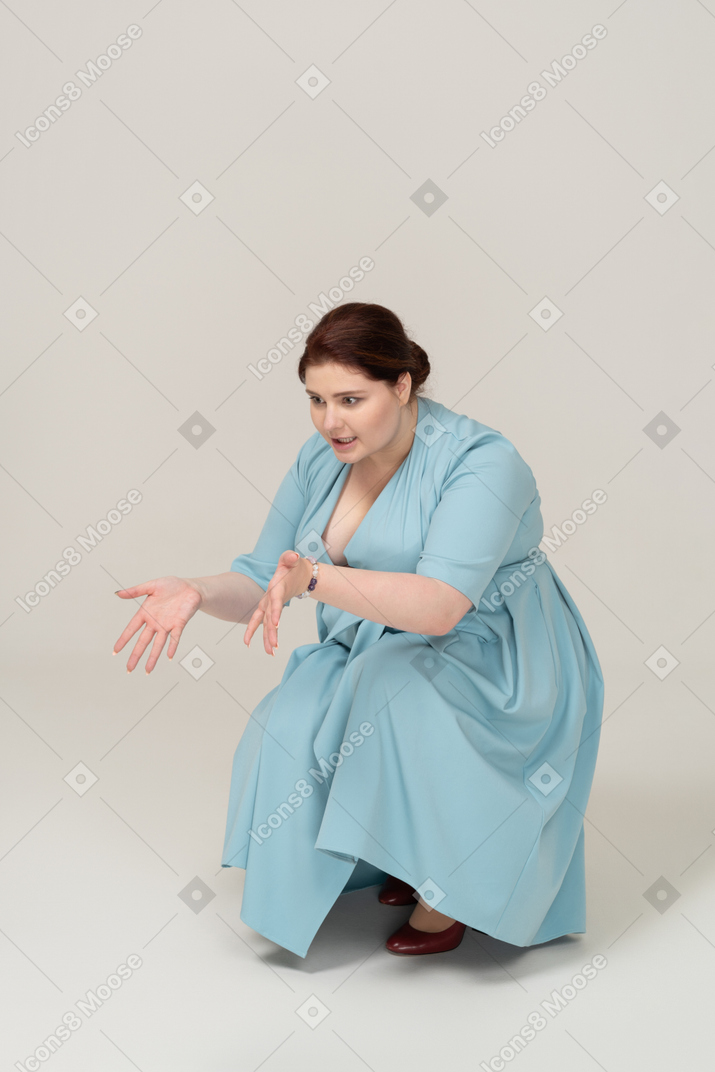 Vista frontale di una donna in abito blu accovacciata