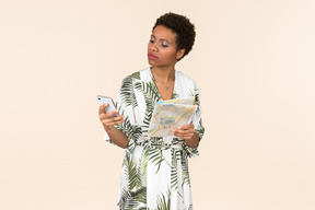 Black short-haired woman in a white and green dress, standing with a smartphone in her hand