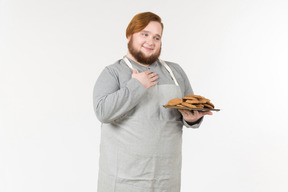 A fat baker with plate of cookies looking pleased