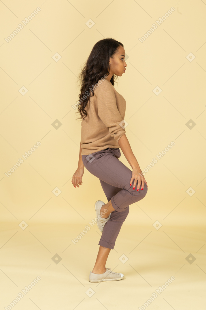 Vista lateral de uma jovem mulher de pele escura tocando seu joelho