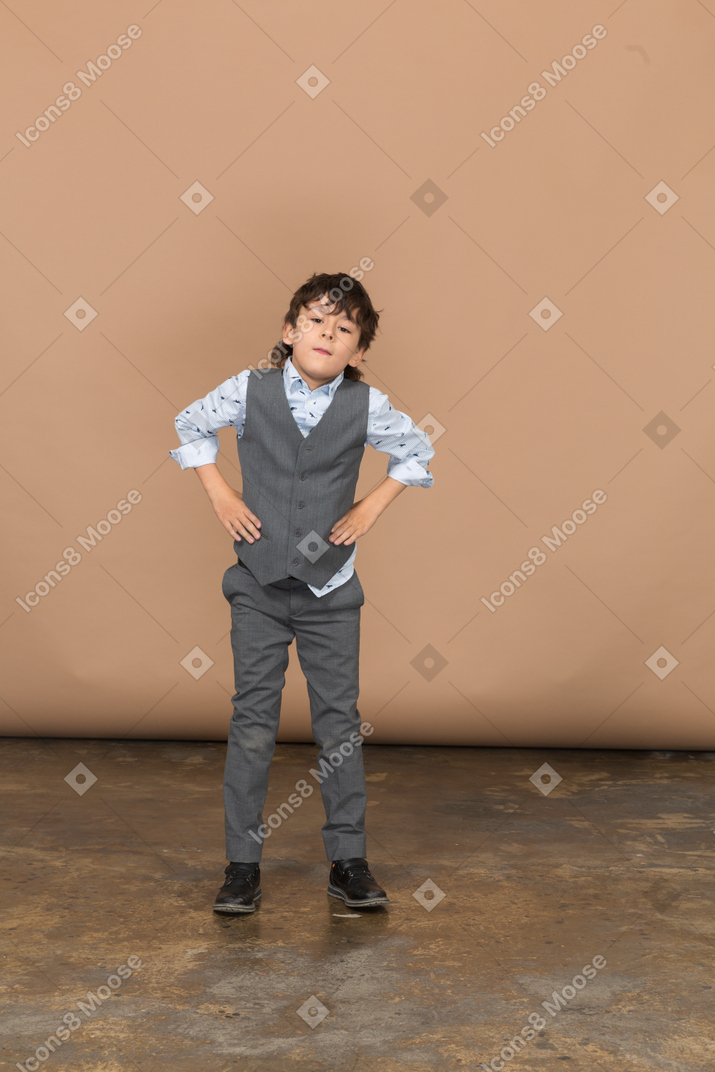 Vorderansicht eines jungen im grauen anzug, der mit den händen auf den hüften steht