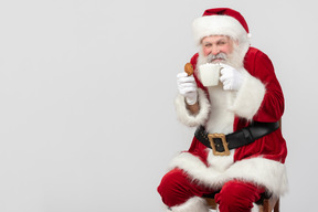兴奋的圣诞老人喝着茶，拿着饼干