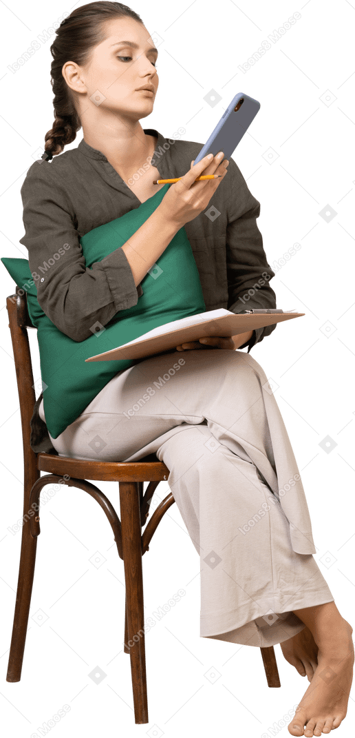 Front view of a thoughtful young woman sitting on a chair with a tablet while checking her phone