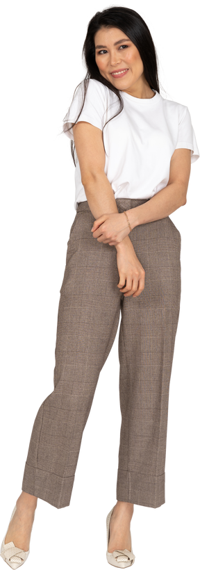 Vista frontal de uma jovem sorridente e tímida de calça e camiseta de mãos dadas