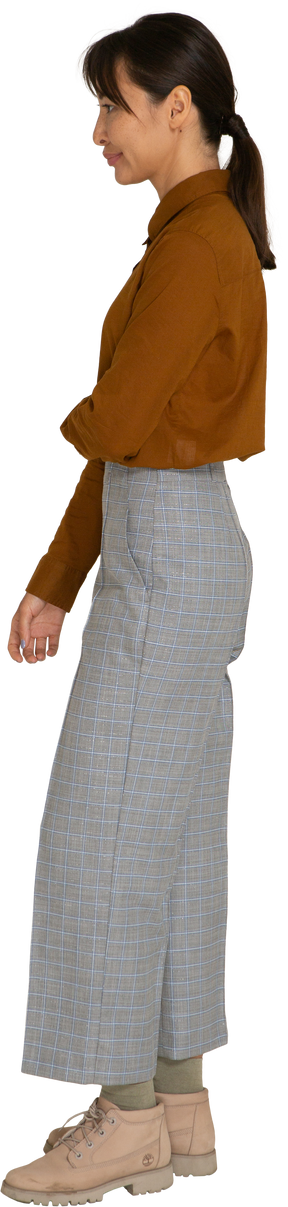 Vista laterale di una giovane donna asiatica imbronciata in calzoni e camicetta che le tiene il braccio