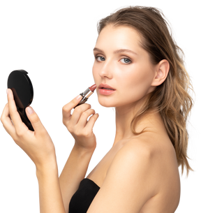 Vista lateral de una mujer joven aplicando lápiz labial mientras sostiene un espejo