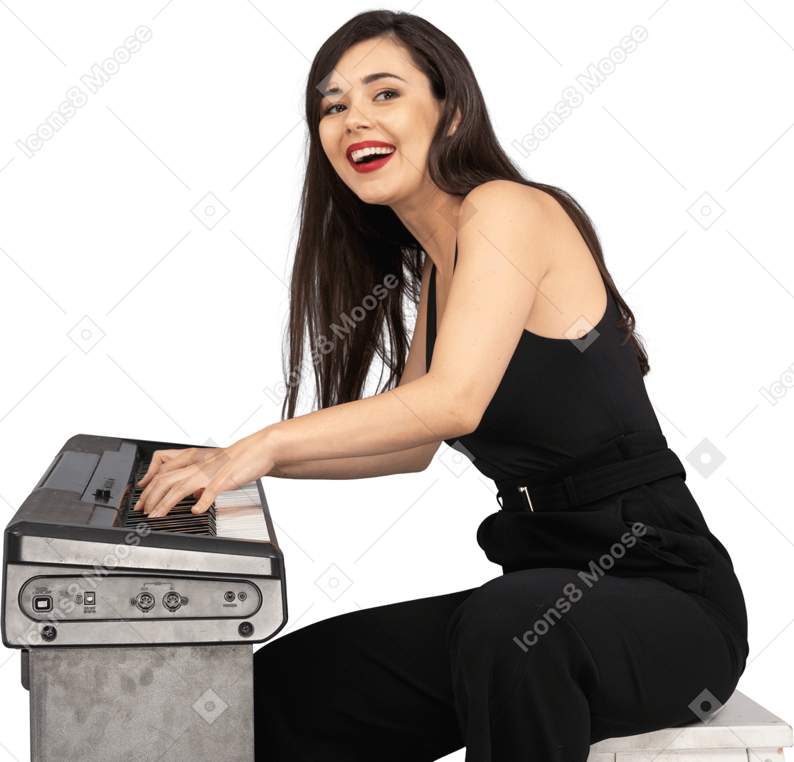 Vista lateral de uma jovem sorridente sentada de terno preto enquanto toca piano