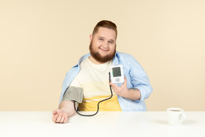 Sorrindo jovem homem com excesso de peso, verificação de pressão arterial