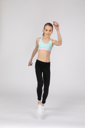 Vista frontal de uma adolescente em roupas esportivas levantando a mão e pulando