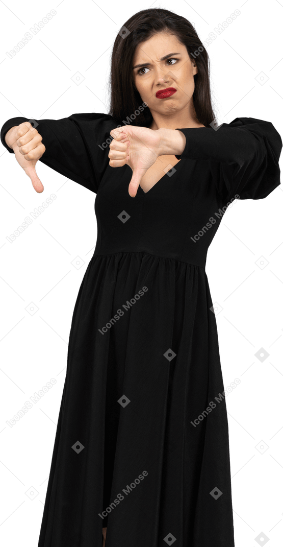 Three-quarter view of a displeased young lady in black dress putting thumbs down