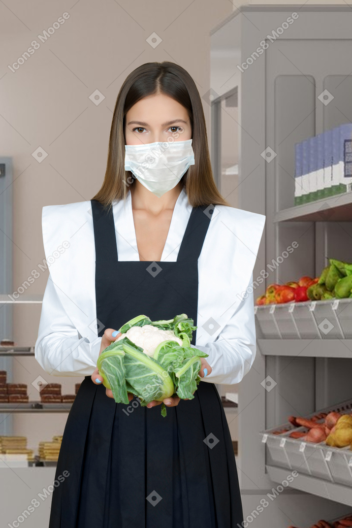 Молодая женщина в масках держит овощ в руках