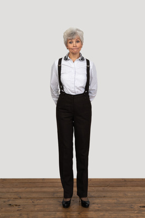 Vista frontal de una vieja mujer disgustada en ropa de oficina haciendo muecas con las manos detrás de la espalda