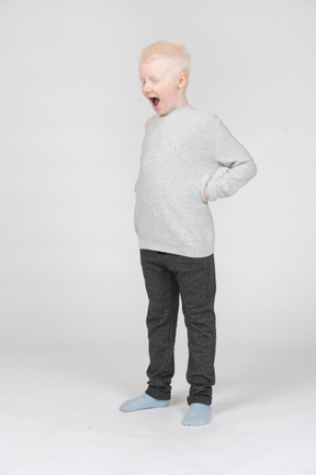 Three-quarter view of a kid boy screaming while putting hands on hips