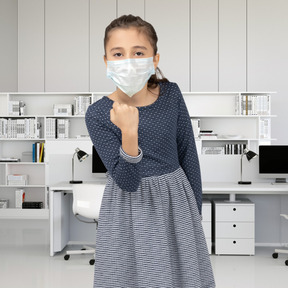 Kleines mädchen in gesichtsmaske, das mit einer geballten faust droht