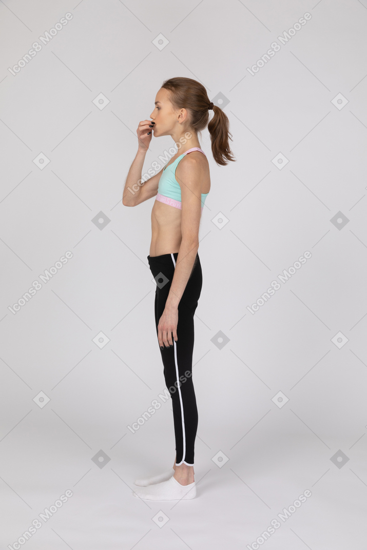 Vista lateral de uma adolescente em roupas esportivas tocando a boca