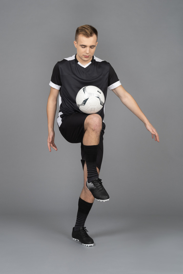 Three-quarter view of a male football player raising leg and kicking a ball