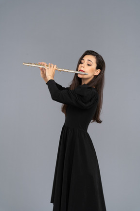 Three-quarter view of a serious young lady in black dress playing the flute