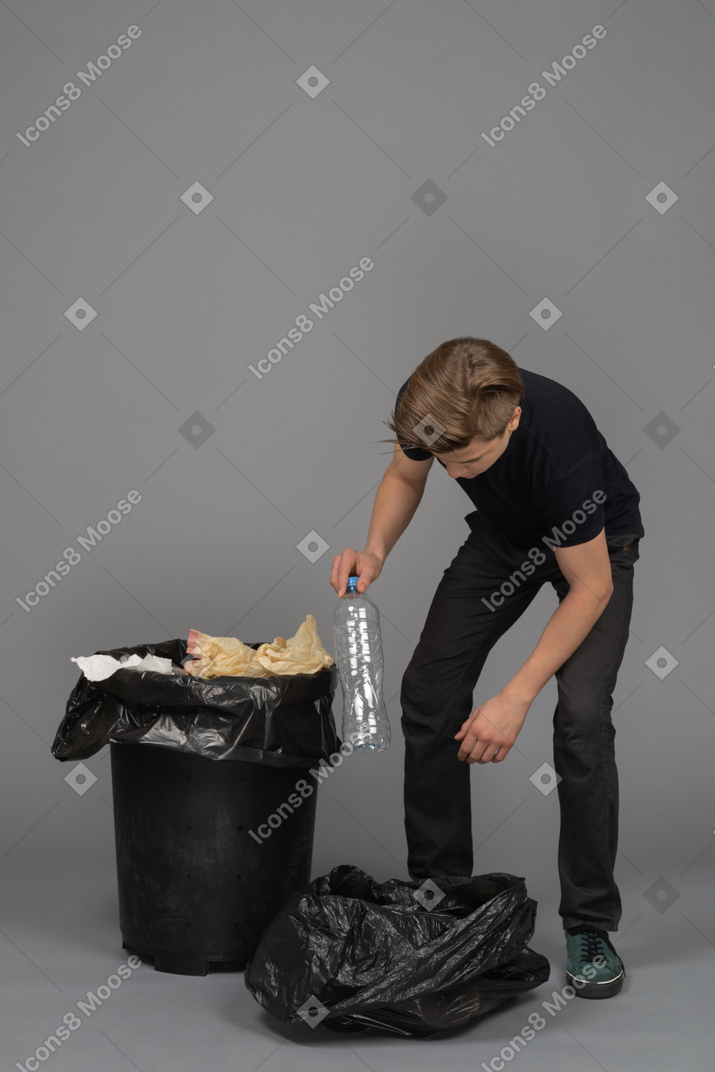 A young man loading a plastic bottle in a trash bag