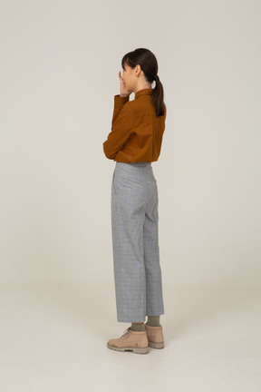 Vista posteriore di tre quarti di una giovane donna asiatica in calzoni e camicetta che le tocca il viso