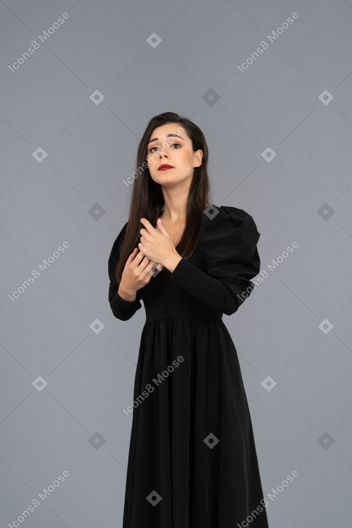Вид спереди серьезной молодой женщины, поправляющей свое черное платье