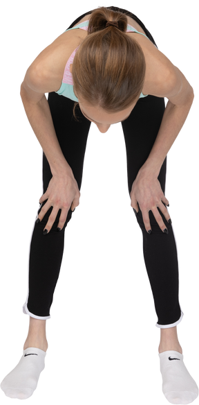Vista frontal de uma adolescente em roupas esportivas inclinando-se para a frente e tocando as pernas