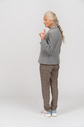 Rear view of an old lady in suit showing ok sign