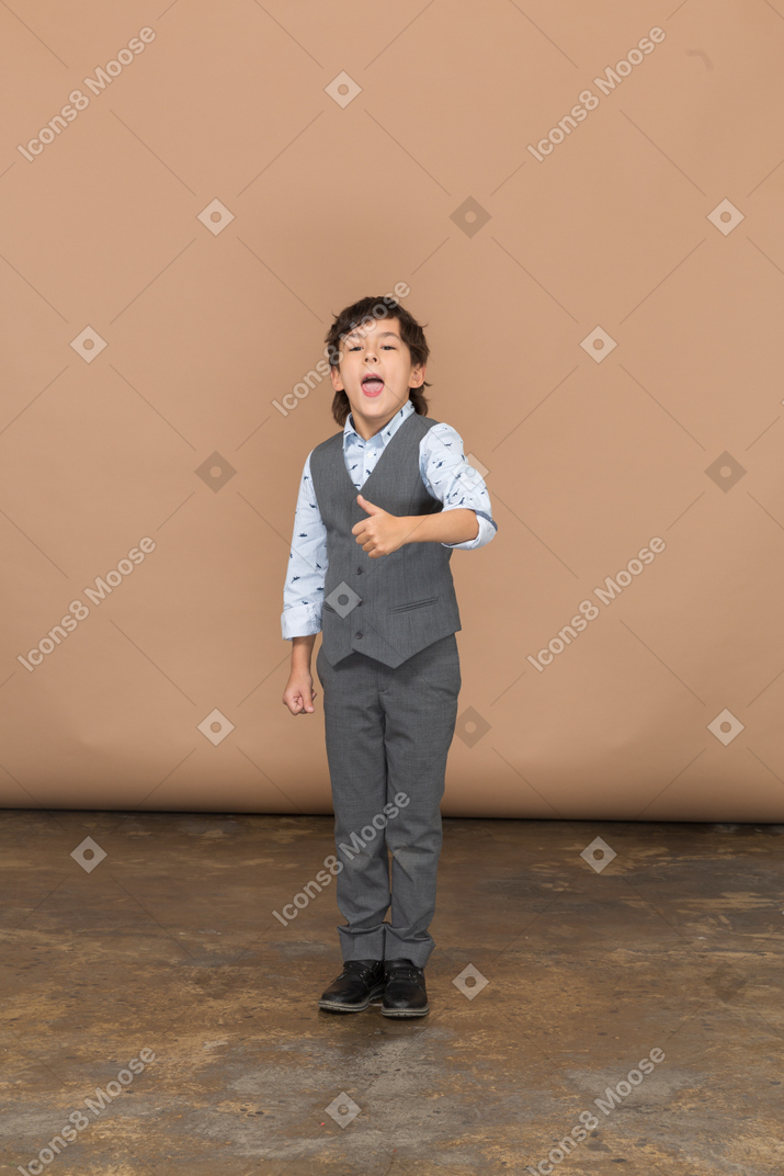 Front view of a cute boy in grey suit showing thumb up