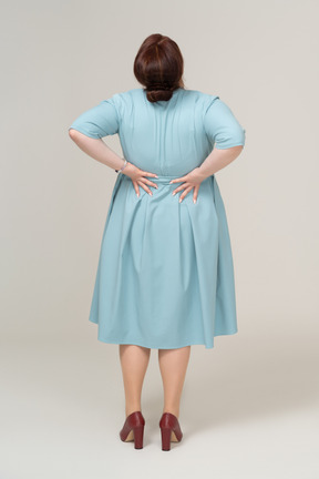 Vista posteriore di una donna in abito blu che soffre di dolore nella parte bassa della schiena