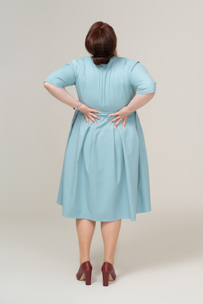 Rear view of a woman in blue dress suffering from pain in lower back