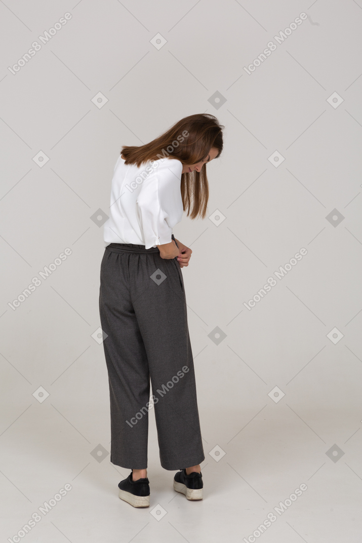 Vista posterior de una señorita en ropa de oficina ajustando sus pantalones