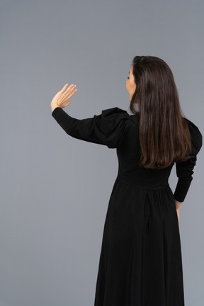 彼女の手を上げている黒いドレスを着た若い女性の背面図