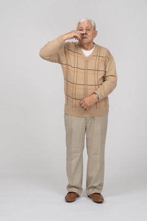 Vista frontal de um velho em roupas casuais, tocando o nariz