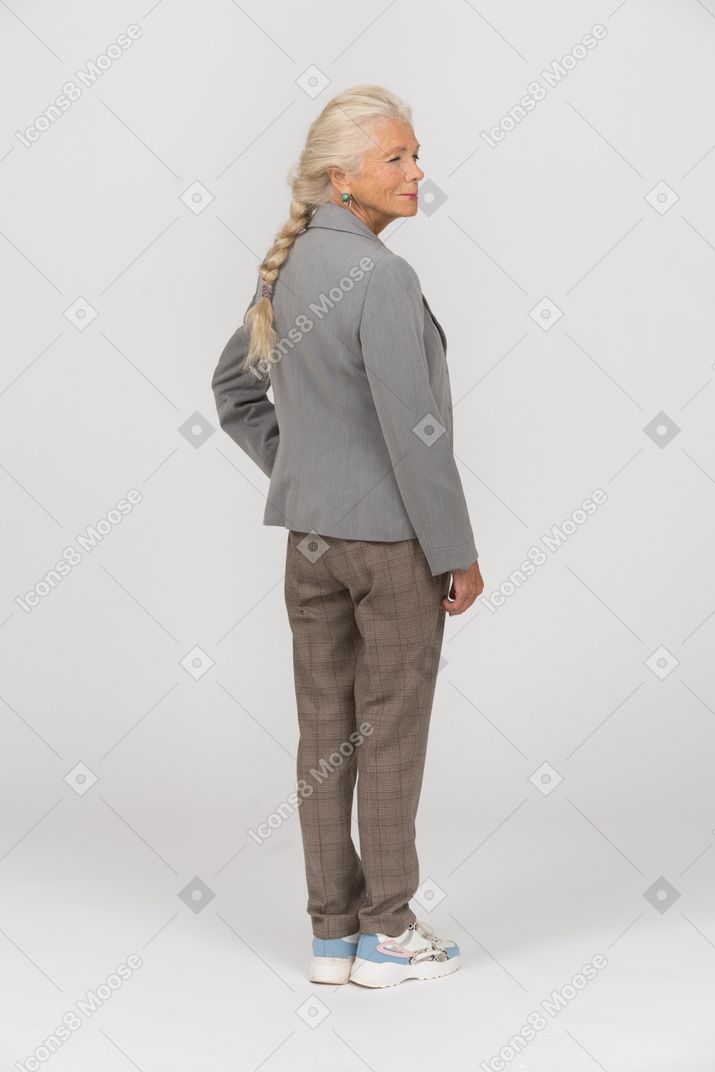 Vue arrière d'une vieille femme en costume posant avec la main sur la hanche