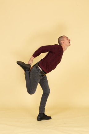 Side view of a young man in red pullover stretching his leg